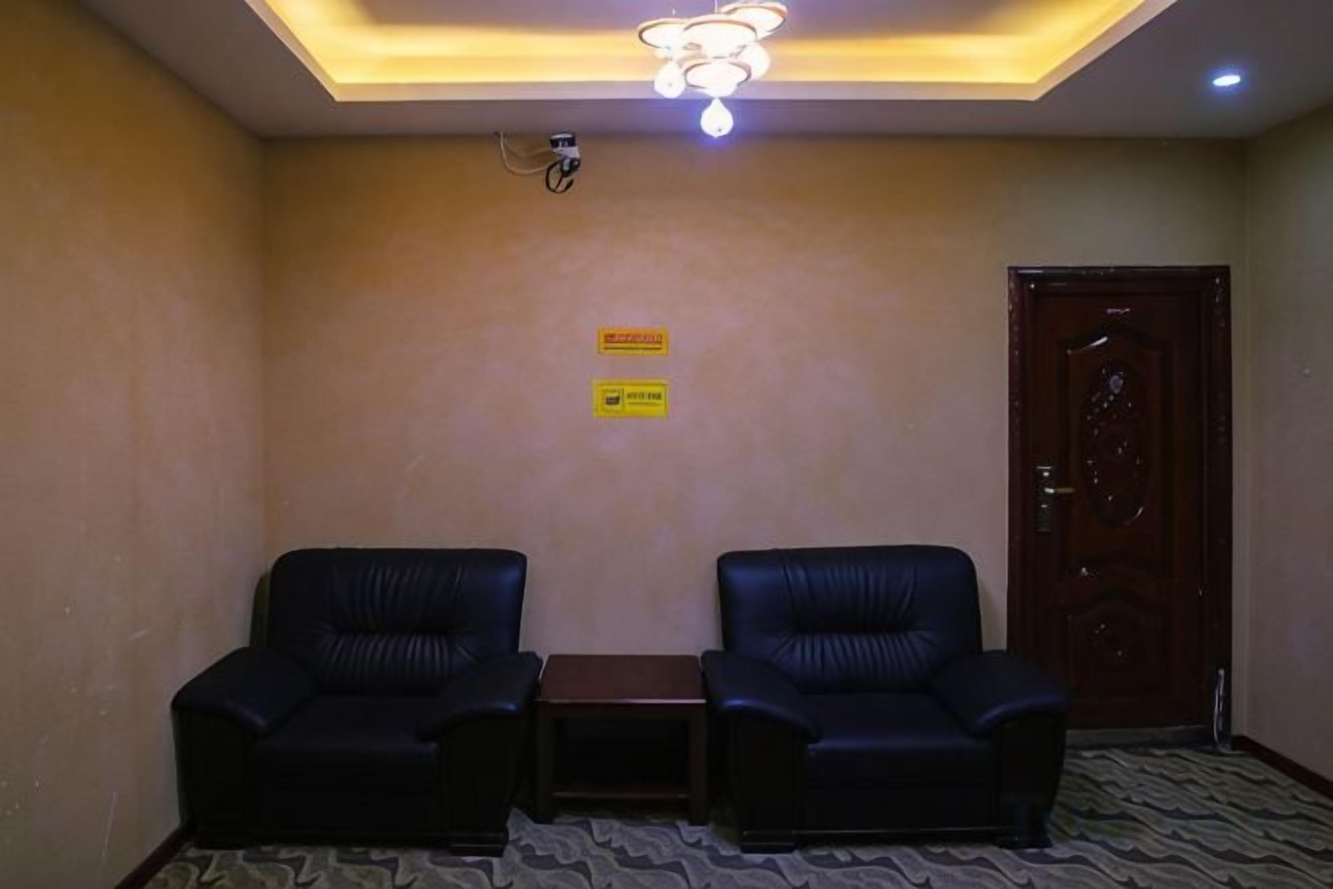 Una habitación con dos sillones de cuero negro, una mesita, una puerta de madera y una lámpara en el techo.