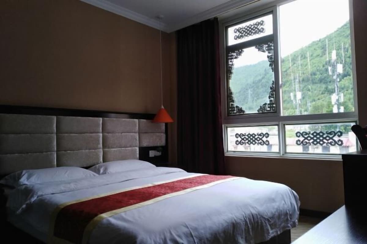 Une chambre d’hôtel avec un lit, une fenêtre ornée de motifs en fer forgé et une vue sur un paysage montagneux.