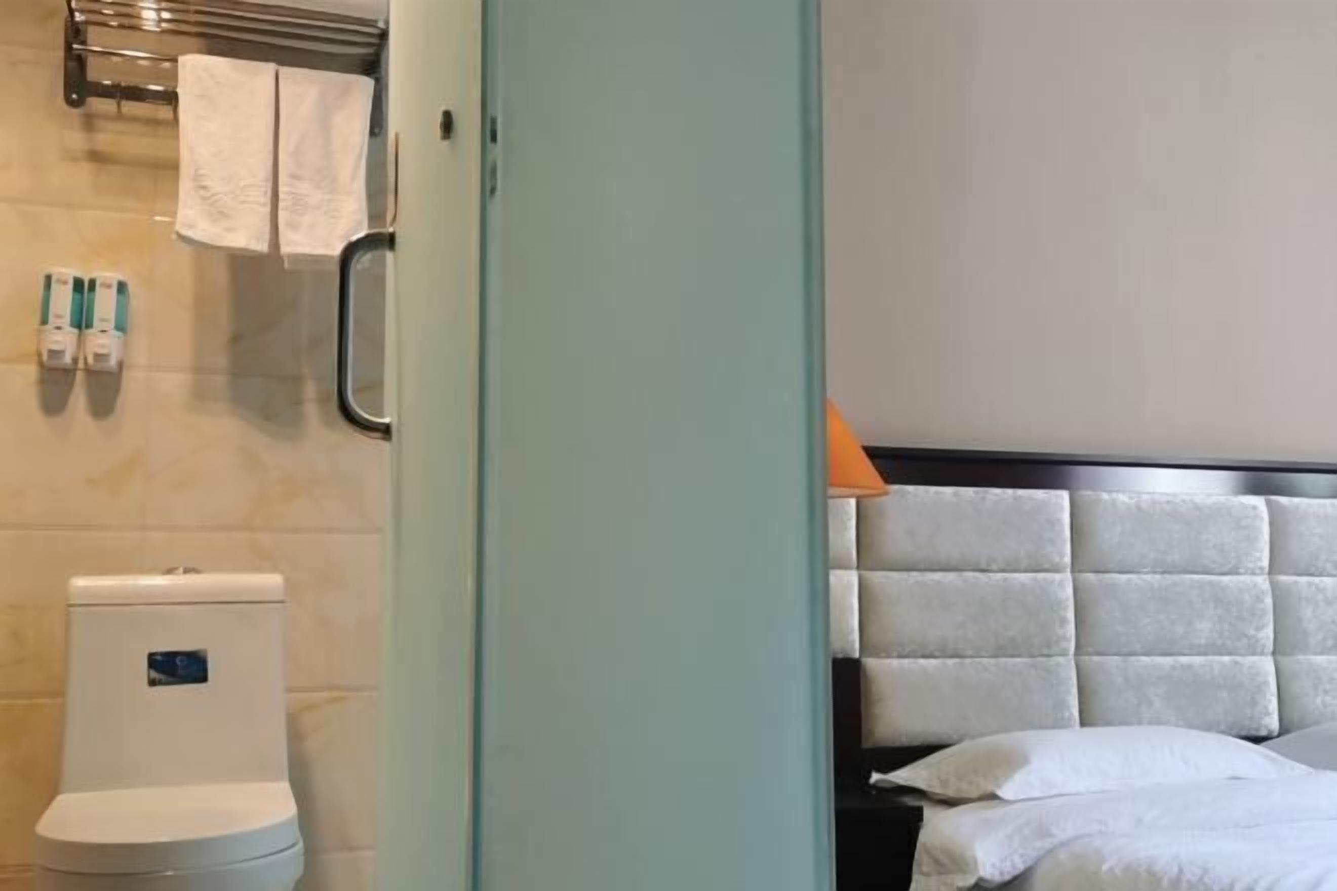 Habitación de hotel con inodoro, toallero y cama con cabecera.