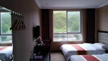 Une chambre d’hôtel avec deux lits, un bureau avec une chaise, une télévision et une grande fenêtre donnant sur des collines.