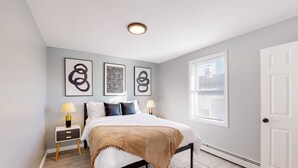 A bedroom with a bed, bedside tables, a window, and artwork on the wall.