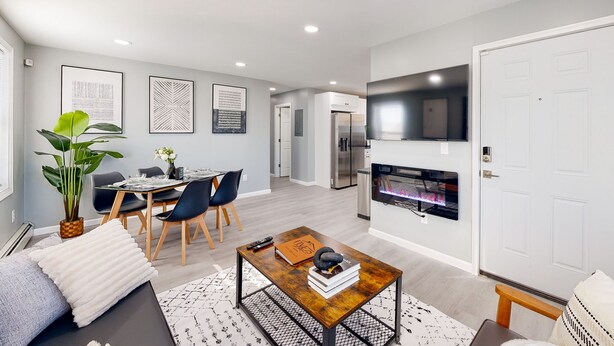 A modern living room with a dining area, a fireplace, and a TV mounted on the wall.