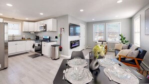 A modern kitchen with white cabinets, a stainless steel refrigerator, and a dining area with a black table set for four.
