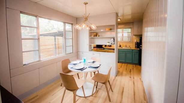 Una cocina moderna con armarios blancos, un comedor con una mesa redonda y sillas, y vistas al exterior a través de amplios ventanales.