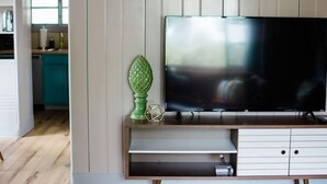 Un salón moderno con un televisor de pantalla plana sobre un mueble de madera, un jarrón decorativo verde, y una cocina visible al fondo.