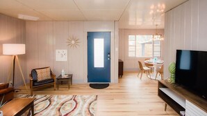Una sala de estar moderna con una puerta azul, un televisor y un comedor con una mesa y sillas.