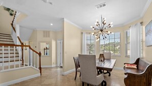 A spacious dining area with a wooden table, chairs, and a unique chandelier. A wooden staircase with white railings leads to another room. - Luxury Family Getaway (Naples)
