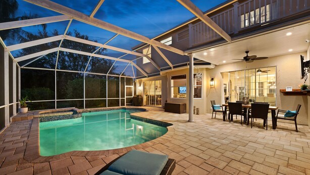 A covered outdoor swimming pool area with a patio, seating, and a view of the house. - Luxury Family Getaway (Naples)