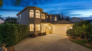 A two-story house with a garage, surrounded by well-maintained landscaping and a clear sky. - Luxury Family Getaway (Naples)