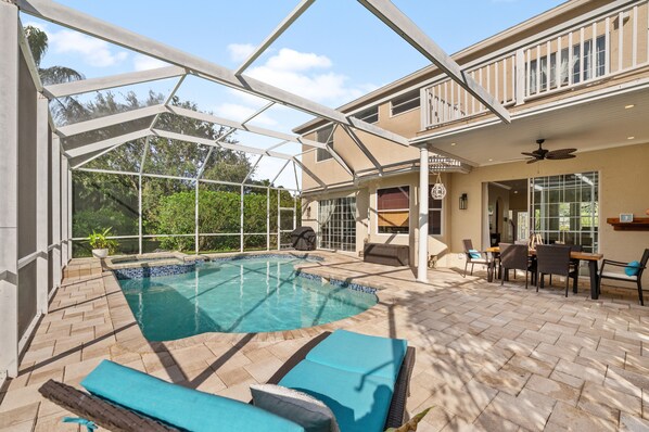 A covered outdoor swimming pool with lounge chairs, a dining area, and a ceiling fan. - Luxury Family Getaway (Naples)