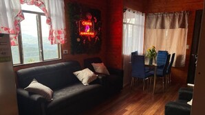 Ein gemütliches Zimmer mit einer schwarzen Couch, einem Esstisch mit Stühlen und einem Neonzeichen an der Wand.