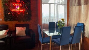 Ein gemütlicher Raum mit Holzvertäfelung, ein Glastisch umgeben von blauen Stühlen, eine Ledersofa und ein leuchtendes Neonzeichen an der Wand.