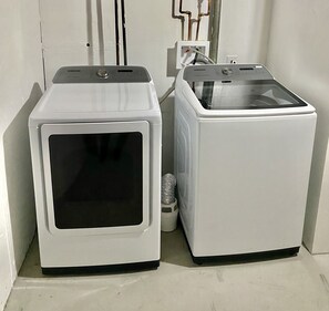 Two white washing machines in a corner with visible plumbing.