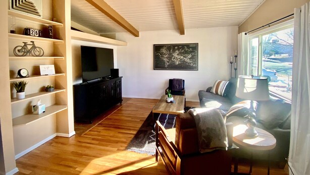 Ett rymligt vardagsrum med trägolv, en soffa, ett soffbord och en tv som står på ett tv-bord. Det finns hyllor med dekorativa föremål och en världskarta på väggen.