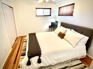 A bedroom with a bed, a nightstand, two windows, and a door. - Central Colorado Springs Mid Century (Colorado Springs)