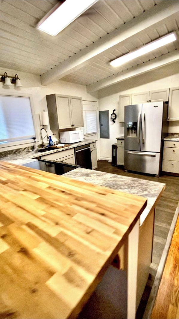 A kitchen with a wooden countertop, stainless steel appliances, and white cabinetry.