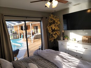 A bedroom with a bed, a dresser, a television, a ceiling fan, and a view of an outdoor swimming pool.