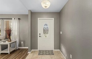 Un pasillo con una puerta blanca, un tapiz estampado y un candelabro.