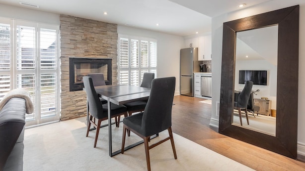 A modern dining area with a stone fireplace, a large mirror, and a kitchen in the background. - Fully Private Apartment - New Luxury Two Bed Private Apartment By The Lake (Mississauga)