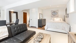 A modern bedroom with a large bed, a dresser, and a desk with a chair. There is a sofa and a coffee table in the living area. - Fully Private Apartment - New Luxury Two Bed Private Apartment By The Lake (Mississauga)