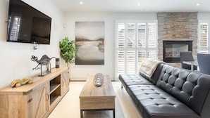 A modern living room with a black leather sofa, wooden cabinet, and a flat-screen TV mounted on the wall. - Fully Private Apartment - New Luxury Two Bed Private Apartment By The Lake (Mississauga)