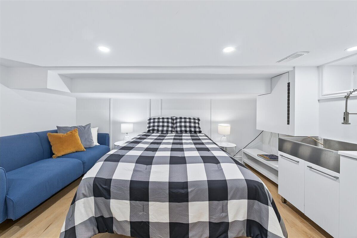 A modern, well-lit room with a bed, a blue sofa, and a kitchenette.