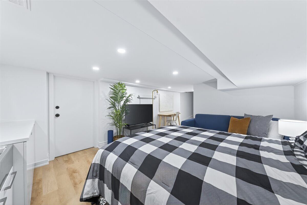 A modern bedroom with a checkered bedspread, a television, a desk, and a plant.
