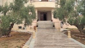 Ein zweistöckiges Gebäude mit einer geschwungenen Fassade, einem Balkon mit Geländer und einem zentralen Eingang mit Treppe.