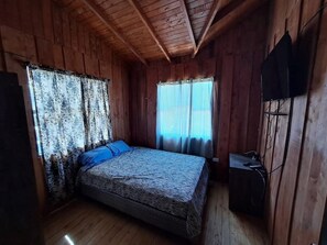 A wooden cabin room with a bed, curtains, and a television.