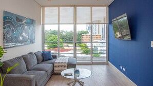 Ein modernes Wohnzimmer mit einem großen Fenster, einem grauen Sofa, einem Glastisch und einem Gemälde an der Wand.