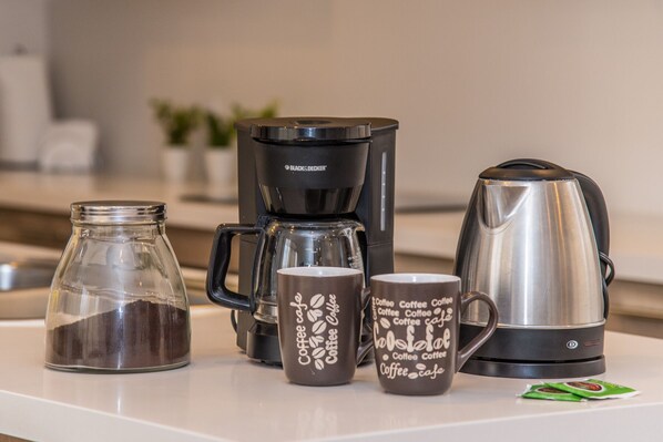 A kitchen counter with a coffee maker, a glass jar, and two coffee mugs.