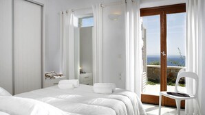 Un dormitorio con una cama grande, una silla y vista al mar a través de un ventanal.