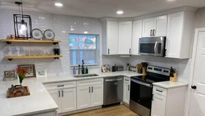 A modern kitchen with white cabinets, a stainless steel oven, and a microwave. - Relax in Style at Our 3BR/2BA Retreat with Private Pool|Game Room|Fire Pit|Yoga (Tampa)