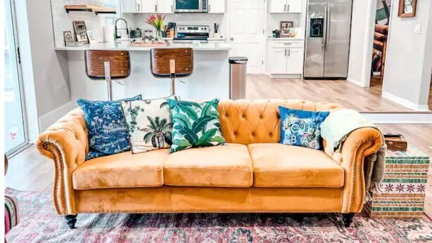 A modern living room with a sofa, a patterned rug, and a kitchen in the background. - Relax in Style at Our 3BR/2BA Retreat with Private Pool|Game Room|Fire Pit|Yoga (Tampa)