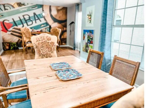 Un comedor con una mesa y sillas de madera, un mantel individual estampado con motivos florales y un mural con la palabra "CUBA".