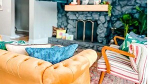 A living room with a stone fireplace, a sofa, and a striped armchair. - Relax in Style at Our 3BR/2BA Retreat with Private Pool|Game Room|Fire Pit|Yoga (Tampa)