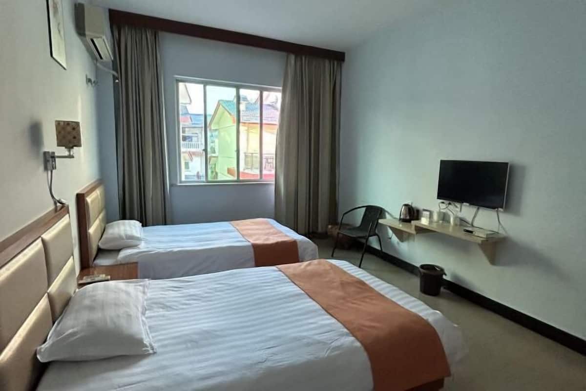 Habitación de hotel con dos camas, un televisor sobre un mueble, una ventana con cortinas y vistas a edificios coloridos.