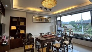 A dining area with a wooden table and chairs, a chandelier, a bookshelf with certificates, and a view of a garden through large windows. - Wuyi Mountain Ruilan Chasu (Wuyishan)