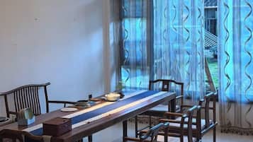 A dining area with a long table, chairs, and a view through a window with patterned curtains.