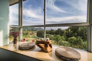 A window with a view of a landscape, a wooden table with a vase and a small plant, and two woven baskets on the windowsill. - Biguan Hall Tea & Inn (Wuyishan)