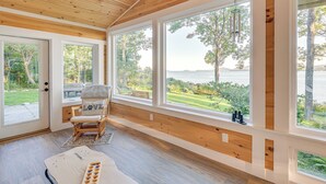 A cozy room with large windows, a wooden ceiling, and a view of a lake. - Oceanfront Frenchman Bay Home: Stunning View! (Lamoine)