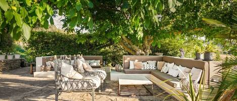 A sunlit outdoor seating area with a metal-framed sofa, a cushioned bench, and a coffee table.