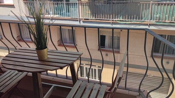 A balcony with a wooden table and chairs, a potted plant, and a view of neighboring buildings. - Feel Welcome Barcelona (Cornella de Llobregat)