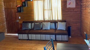 Interior de uma cabana de madeira com um sofá, cortinas e um quadro na parede.