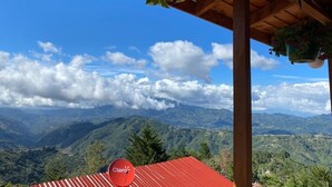 Vista de uma estrutura de madeira com telhado vermelho, com vista para uma paisagem montanhosa.