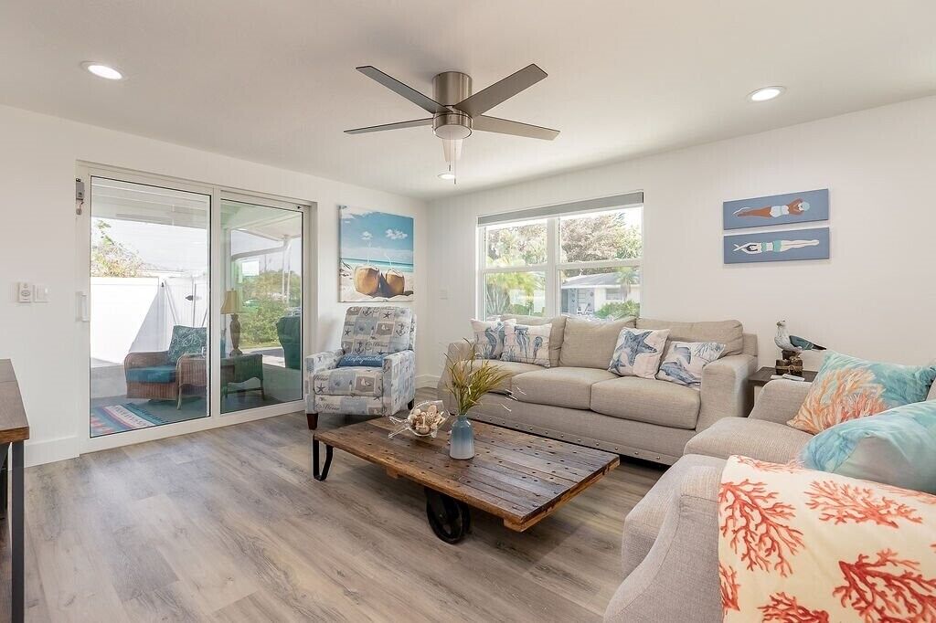 A spacious living room with a ceiling fan, a large window, and a sliding glass door leading to an outdoor area.