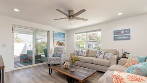 A spacious living room with a ceiling fan, a large window, and a sliding glass door leading to an outdoor area. - Coco Cay - Beautiful totally remodeled 4 bedroom with private pool (Holmes Beach)