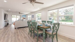 A dining area with a wooden table and matching chairs, a ceiling fan, and large windows offering a view of the outdoors. - Coco Cay - Beautiful totally remodeled 4 bedroom with private pool (Holmes Beach)