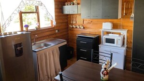 A compact kitchen with wooden walls, a refrigerator, a sink, a microwave, and a small dining area. - Red Princess Cabin - PERFECT view of the valley! (San José)