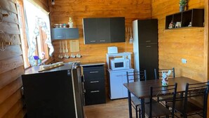 A compact kitchen with wooden walls, a dining area with a table and chairs, and a microwave on a small counter. - Red Princess Cabin - PERFECT view of the valley! (San José)